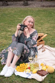 a young woman in a long dress and straw hat is resting on a picnic with fruits, cheese plate and champagne, rest from worries and household chores parks and recreation areas,.High quality photo