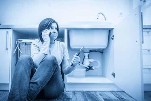 Woman sitting near leaking sink calling for help