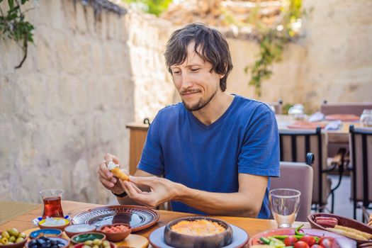 Man eating turkish breakfast. Turkish breakfast table. Pastries. Vegetables. Olives. Cheeses, fried eggs. Jams, tea in copper pot and tulip glasses. Wide composition.