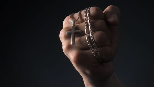 Close-up images of crucifix pendant and necklace in hand on black color background in studio which represent praying for god or jesus and thank gods for giving peaceful and faithful to people