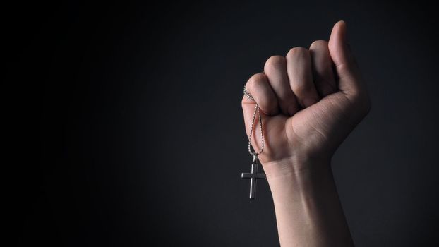 Close-up images of crucifix pendant and necklace in hand on black color background in studio which represent praying for god or jesus and thank gods for giving peaceful and faithful to people