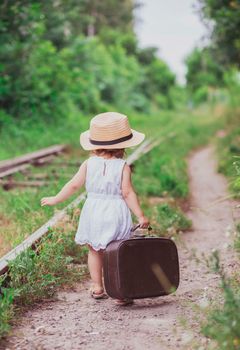 Charming baby with a suitcase walks along the railroad.