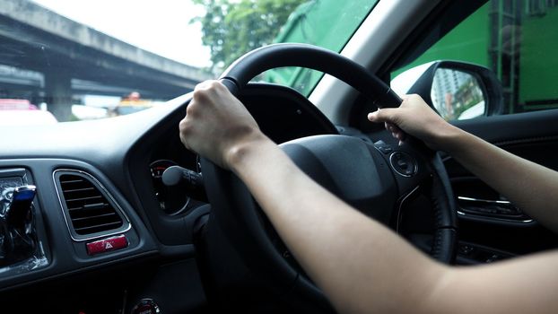 Close-up images of woman hands driving and controling car with confidence and safety which car moving to the Bangkok city Thailand for roadtrip and on the road no traffic jam.