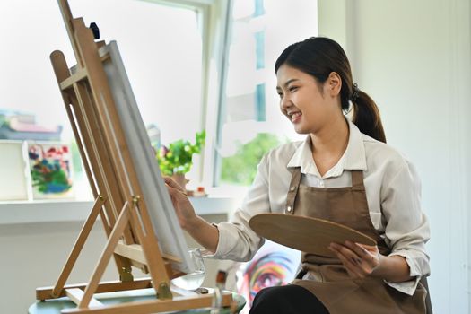 Attractive female artist painting with watercolor on canvas in art workshop. Art, creative hobby and leisure activity concept.