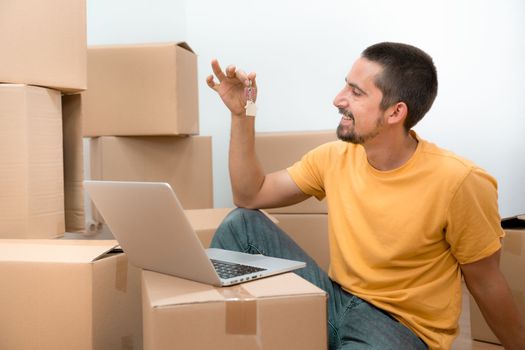 Happy caucasian man with the keys of his new home flat apartment house and laptop between boxes. High quality photo