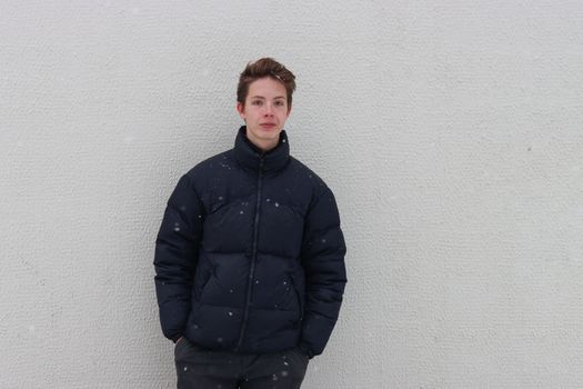 A boy of 14-17 years old stands against the wall and keeps his hands in his pockets.