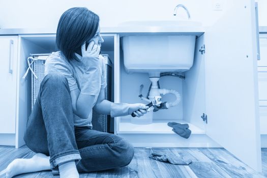 Woman sitting near leaking sink calling for help