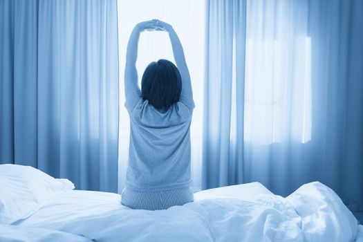 Woman stretching in bed after wake up, back view