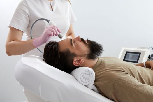 Doctor female dermatologist trichologist makes a procedure to stimulate hair growth to a patient man. Laser treatment of alopecia and hair loss