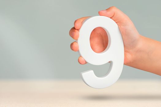 Number nine in hand. A hand holds a white number 9 on a blurred background. Concept with number nine. Birthday 9 years, percentage, ninth grade or day