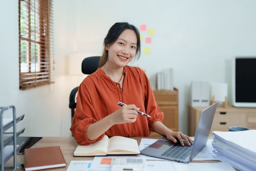 Portrait of a woman business owner showing a happy smiling face as he has successfully invested her business using computers and financial budget documents at work.