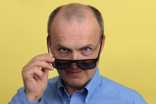 Close-up portrait of a positive man in a blue shirt holding black glasses in his hand looking at the camera.