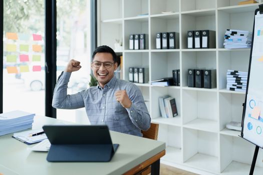 Portrait of a man business owner showing a happy smiling face as he has successfully invested her business using computers and financial budget documents at work.