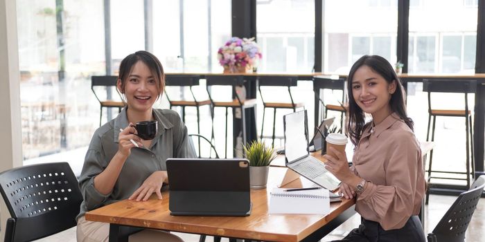 Two young Asian businesswomen show joyful expression of success at work smiling happily with a laptop computer in a modern office...