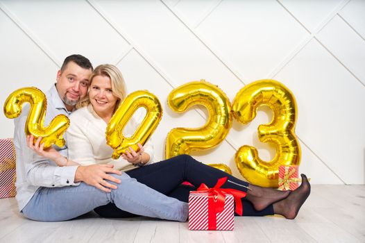 Young couple having romantic date on Christmas eve with 2023 golden foil inflatable balloons. Christmas and 2023 New Year Holidays concept.