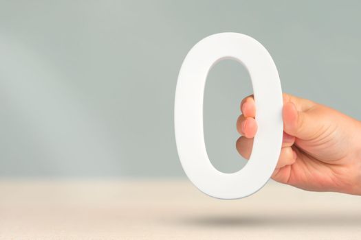 Numeral zero in hand. A hand holds a white number zero on a blurred background with copy space. Zero concept, 0 percent interest rate, minimum air emissions, cost or credit no increase