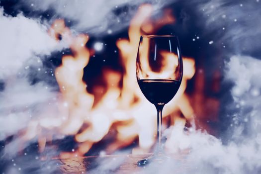 Winter atmosphere and Christmas holiday time, glass of wine in front of fireplace covered with snowy effect on window glass, holidays backgrounds