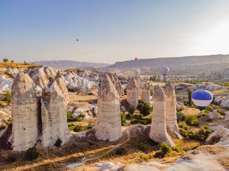 Colorful hot air balloons flying over at fairy chimneys valley in Nevsehir, Goreme, Cappadocia Turkey. Spectacular panoramic drone view of the underground city and ballooning tourism. High quality.