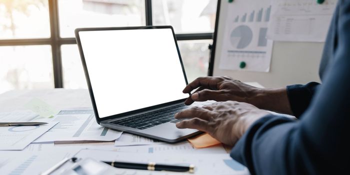 Close-up image, Businessman or male financial consultant working on laptop computer, typing on keyboard, checking the financial data. laptop blank screen mockup...