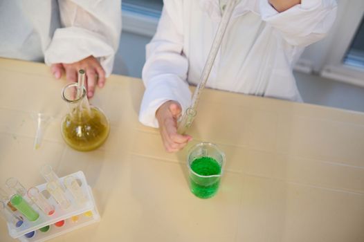 Selective focus: close-up kids performing chemical experiments, using graduated pipette, beaker, test tubes, flasks, chemicals and reagents, in the chemical school laboratory at chemistry class