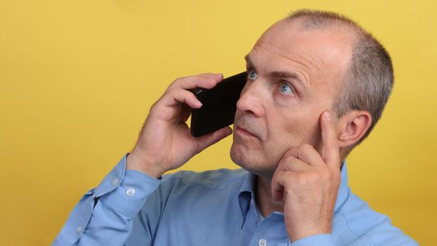 Elderly man with a phone in a blue shirt on a yellow background.