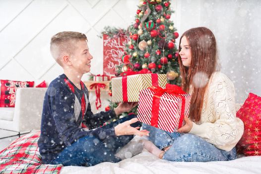 A cheerful teenagers, sister and brother, opens a Christmas gifts. Cheerful Teenagers boy and girl lies in bed with a christmas presents in they hands. Christmas themed background