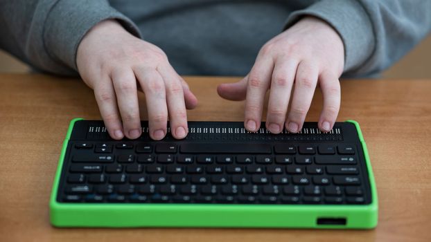 A blind man uses a computer with a Braille display and a computer keyboard. Inclusive device
