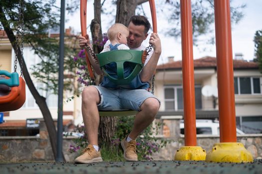 Dad and son swing on a swing. Happy family. The father spends time with the children 