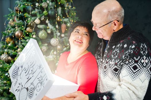 Man 60s giving a Christmas present to his woman. Great xmas surprise Beautiful woman 60s opening a gift box and smiling while her boyfriend hug her. Christmas wonder concept