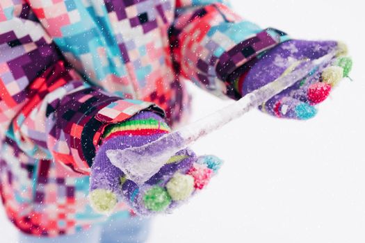 Close up of child girl hands holding icicle. Kid spending time outside and environments provide wonderful hands-on experiences in nature during the winter. Winter activities for kids. Woolen mittens.
