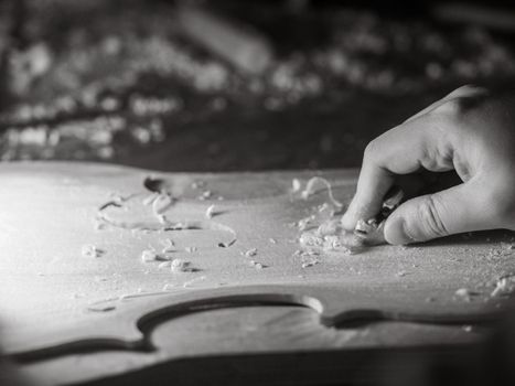 luthier working on raw wood violin plate with finger plane on the bench