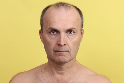 A man 45-55 years old without clothes with a hairy chest on a yellow background.