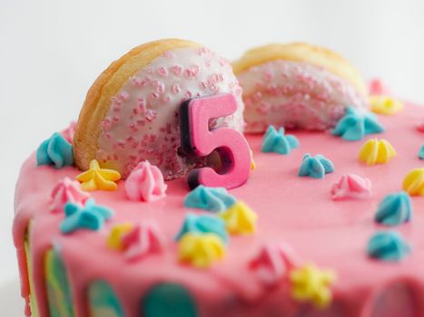 Close up of pink frosted dripping cake with donut and plastel brushed royal star sprinkles insolated on white studio shot