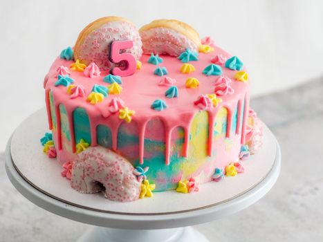 Close up of pink frosted dripping cake with donut and plastel brushed royal star sprinkles insolated on white studio shot