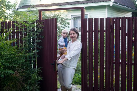 Curious woman with a baby opening the gate of fence and looking at camera welcoming friends