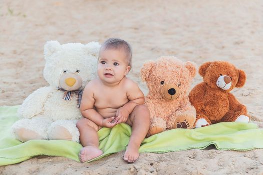 beautiful baby sitting with teddy bears on the beach.