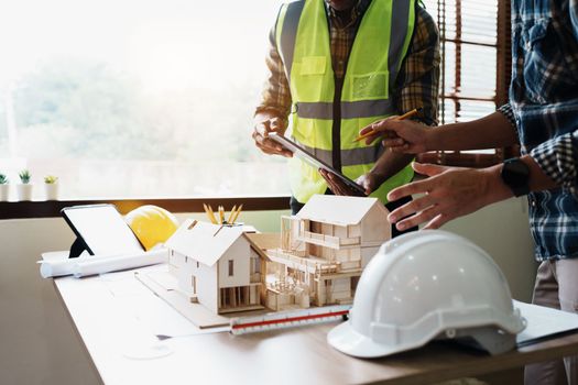 Engineers are consulting the team to design an architectural structure for clients with blueprints and building models to work at office.
