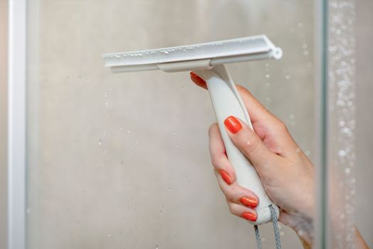 Shower cabin cleaning. Cleaning glass after using the shower. Cleaning glass with a rubber scraper