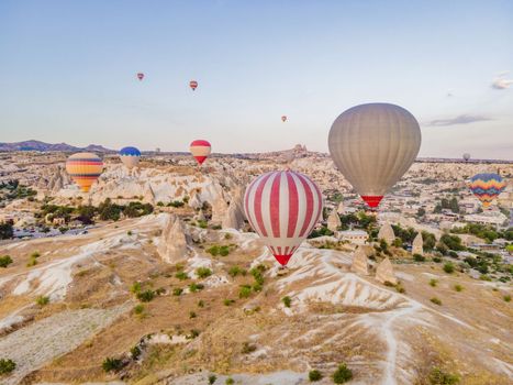 Colorful hot air balloons flying over at fairy chimneys valley in Nevsehir, Goreme, Cappadocia Turkey. Spectacular panoramic drone view of the underground city and ballooning tourism. High quality.