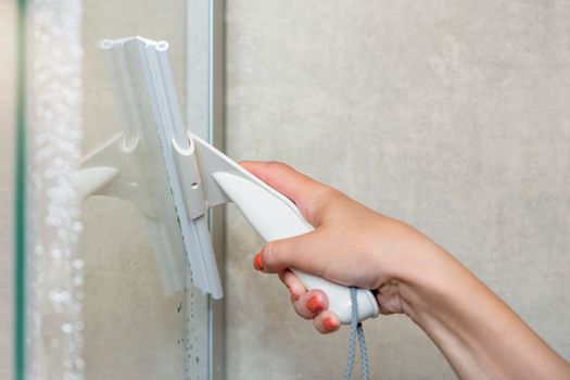 Shower cabin cleaning. Cleaning the glass wall of the shower cabin with a glass scraper. cleaning the house, taking care of the bathroom and shower