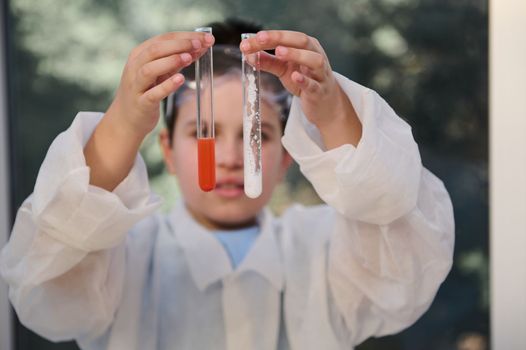 Details: test tubes with chemicals in the hands of blurred schoolboy, chemist scientist in white lab coat, examining features of substances inside test tubes, conducting experiments at chemistry class
