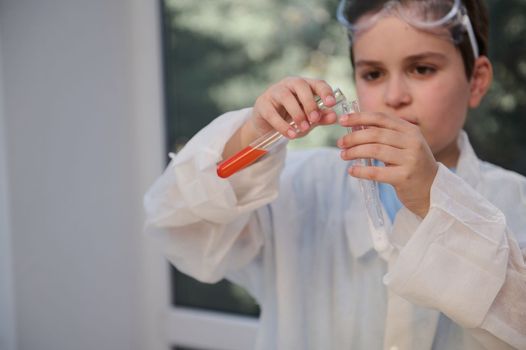 Close-up of a schoolboy's hands holding test tubes with chemicals and reagents at chemistry class in school scientific laboratory. Teenage boy, inspired, young chemist scientist conducts experiments