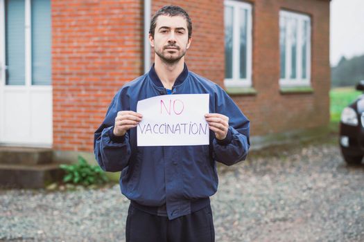 Man holding anti-vaccination poster near his house.