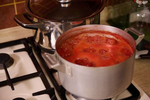 Close-up of tomato juice boiling in metal saucepan on the stove. Preparing homemade passata from organic ripe harvested juicy tomatoes, according to Italian traditional recipe. Canning food for winter