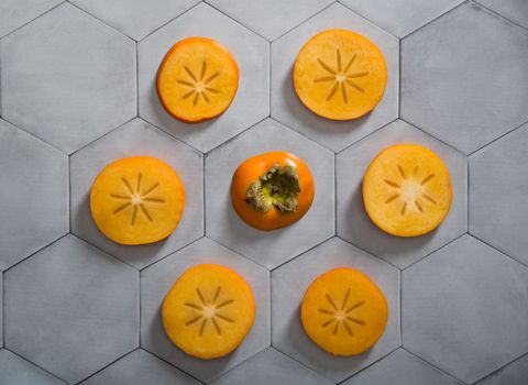 Persimmon slices lie on a gray background in the form of a hexagonal tile, colorful food, flatley fruits. High quality photo