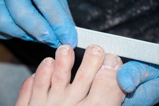 The pedicure master grinds the toenails of clients with a nail file, polishes polishing the nail plate with a buff, High quality photo