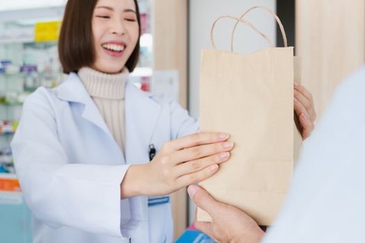 Affable pharmacist give or handing customer a bag of qualified medications or medical supplies, customer service concept in pharmacy. Pharmacist working on cashier talking to customer in drugstore.