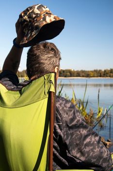 Young unrecognizable guy fisherman catches fish sitting in a chair on the bank of a river or lake. The angler sits on a chair with fishing tackle. A perfect holiday by the river with a fishing rod