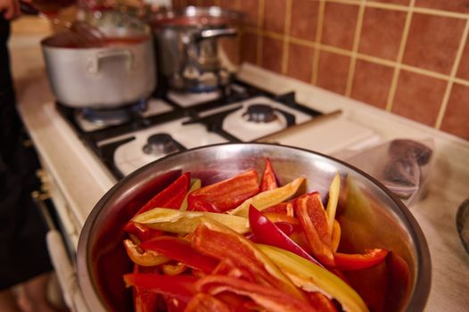 Selective focus on chopped raw sweet and colorful bell peppers on metal bowl on a kitchen coutertop. Healthy food. Canning vegetables. Step-by-step conserving harvested crop of organic vegetables