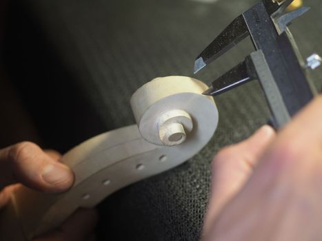 violin maker using a meter to shape and accurate measure fiddle scroll